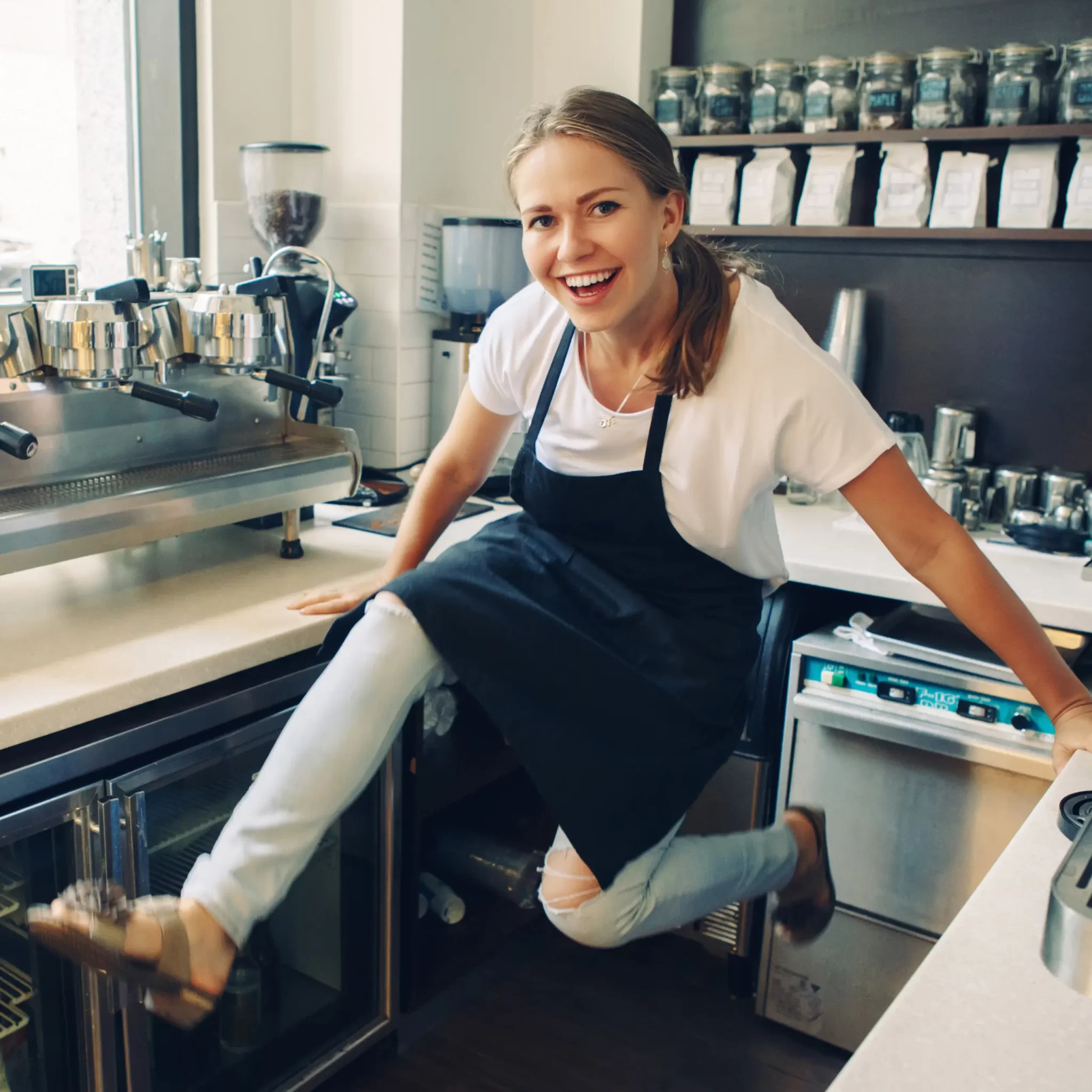 A photo of a female barista swinging her legs up and having fun in the cafe. 